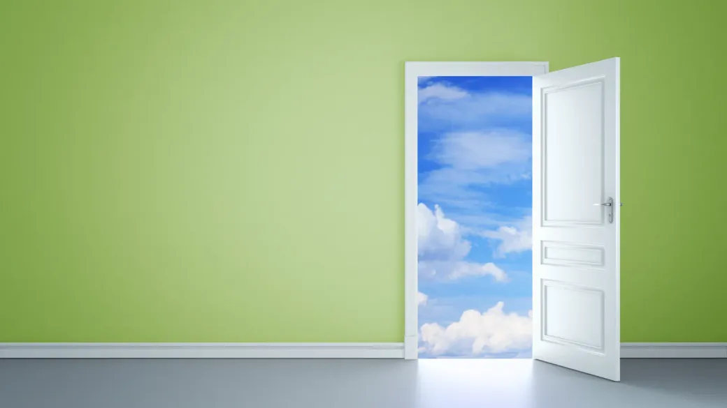 Eine offene Tür in einer grünen Wand führt in einen blauen Himmel mit Wolken